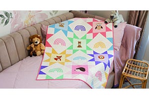 Zoo Crew baby quilt featuring pastel star blocks and appliqué zoo animals, draped over a nursery chair in a soft, modern nursery setting.
