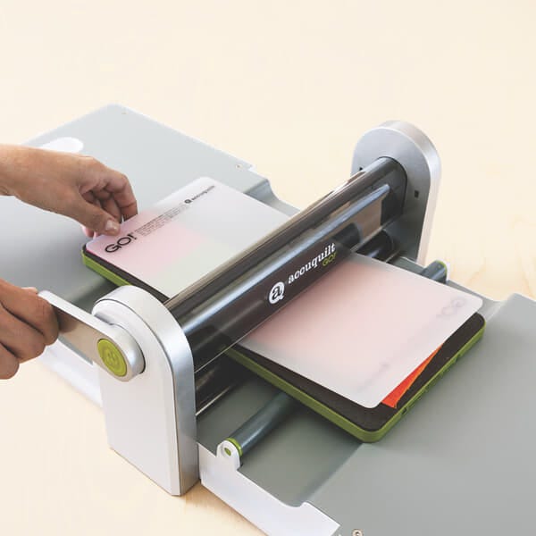 image of hands rolling the die, fabric and cutting mat through GO! Fabric Cutter