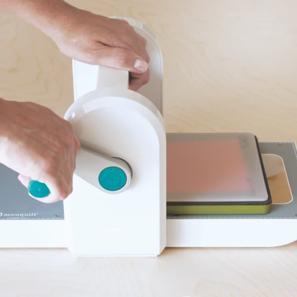 image of hands rolling the die, fabric and cutting mat through GO! Me Fabric Cutter