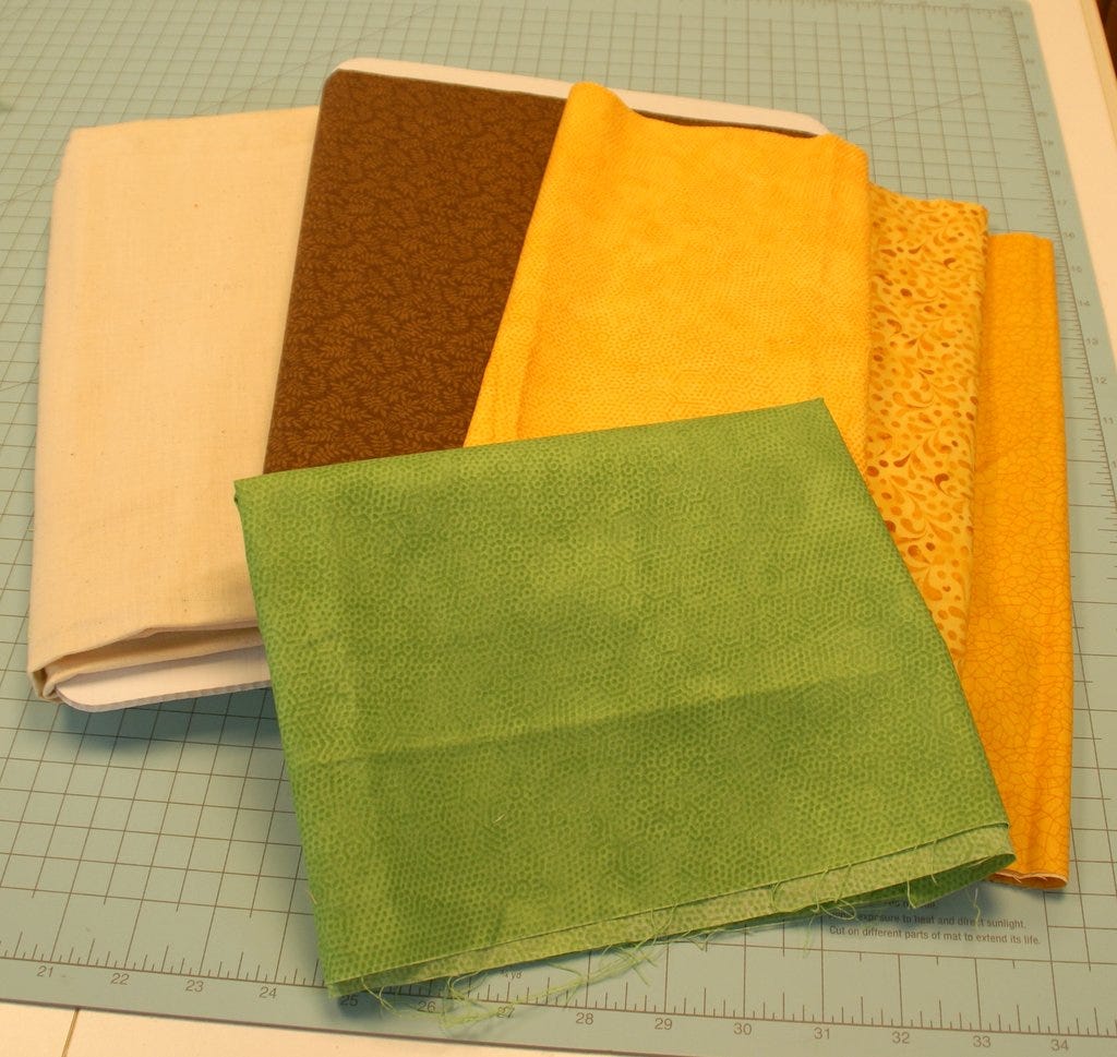 quilt cotton fabric in green, brown and various shades of yellow on a self-healing quilting cutting mat