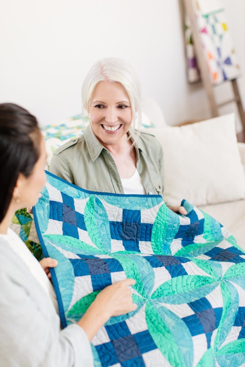 A quilt owner inspects a quilt with another person.