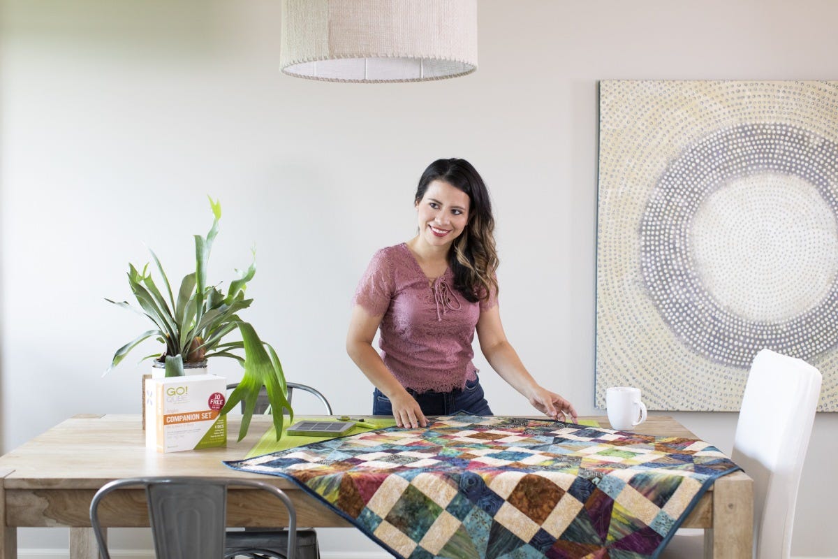 A person standing and smiling next to a quilt on a table.