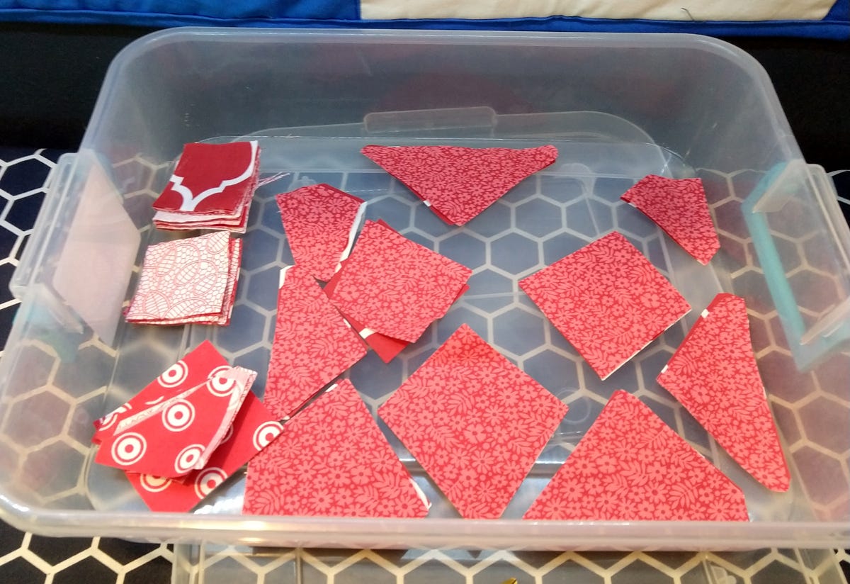 plastic storage tub with various red print fabric cut in triangles, squares and wonky heart pieces 