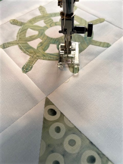 close up of accuquilt ship's wheel fabric applique piece on white block center with sewing machine straight stitching edges