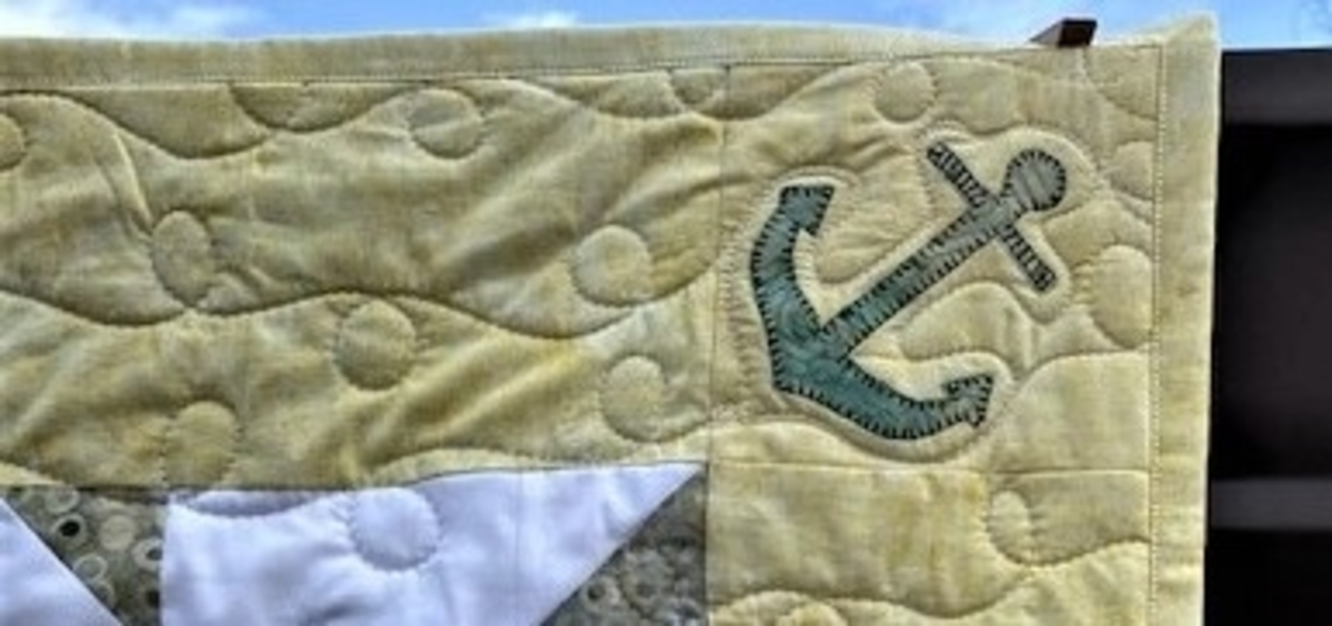 close up of finished baby quilt with accuquilt go! nautical medley anchor applique corner piece with curly quilting
