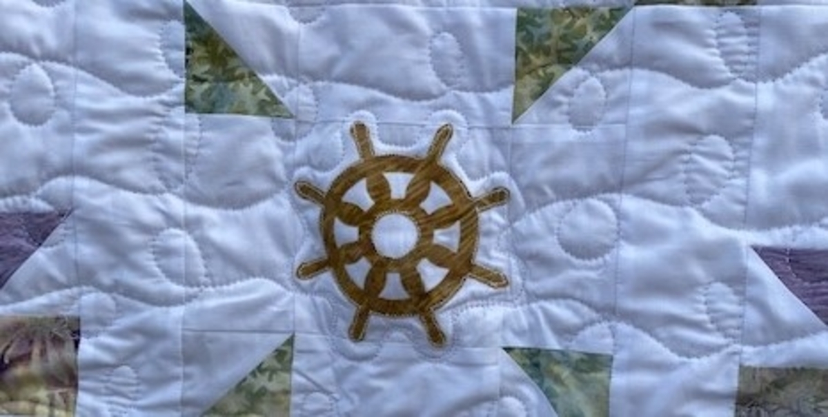close up of ship's wheel appliqued to the center of baby quilt with curly quilting